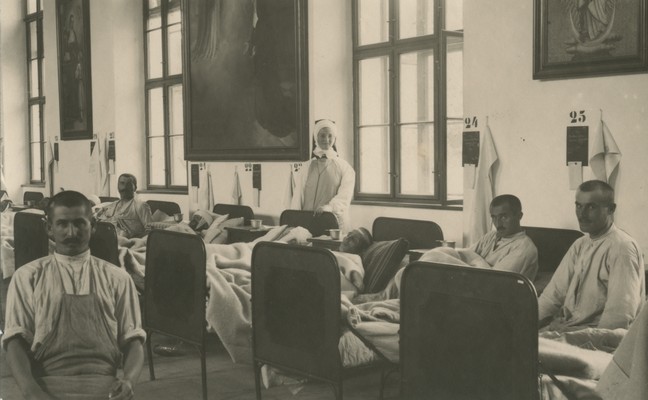 Ranjeni vojaki v poljski bolnišnici 7/4, ki je od avgusta 1915 do junija 1916 delovala na škofjeloškem gradu. Nad vsako posteljo visi tablica s podatki o ranjencu in njegovi poškodbi ali bolezni.